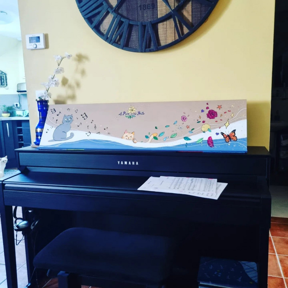 Support à partition décoré avec un chat assis et souriant sur la gauche, un chat espiègle au milieu, et une vague de notes de musique qui part de la gauche et se transforme progressivement en plein de décorations (fleurs, papillons...) vers la droite