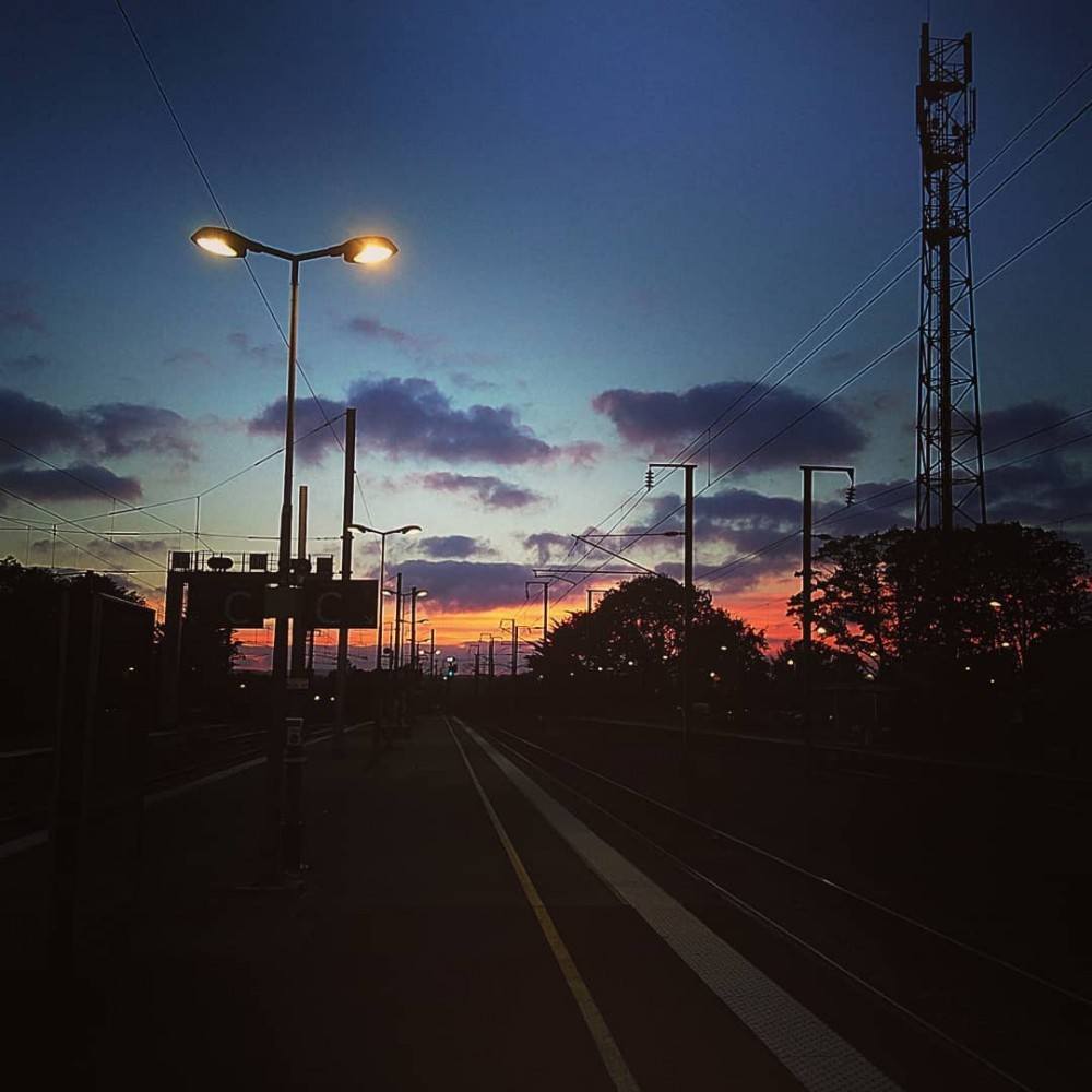 Coucher de soleil sur le quai d'une gare, avec un lampadaire allumé