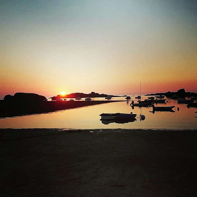 Photo du soleil qui se couche au loin, plage et bateaux